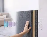 Mano tocando material para aislar ruido. Gráfico de sonido muestra cómo se reduce.