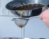 Se cuela aceite rancio de una sartén a través de un colador fino, cayendo en un recipiente.