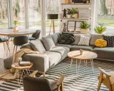 Un salón moderno y acogedor con sofá gris, alfombra de rayas, mesa de centro de madera y grandes ventanales que dejan entrar la luz natural.