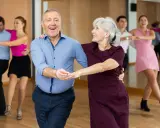 Uśmiechnięta para seniorów uczy się, jak tańczyć na 3, w tle inne pary.