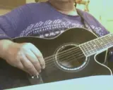 Main d'un musicien ajustant l'accordage 12 cordes d'une guitare acoustique noire.