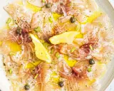 Délicieux carpaccio de saumon, fines tranches de poisson cru arrosées d'huile d'olive, garnies de câpres, oignons rouges et quartiers de citron.
