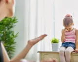 Smutna dziewczynka siedzi przy oknie, a jej mama gestykuluje. Warto nauczyć się, jak przestać krzyczeć na dziecko, by budować lepsze relacje.