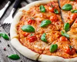 Pyszna pizza Margherita, klasyka włoskiego jedzenia, z pomidorkami koktajlowymi i bazylią na drewnianym blacie.