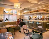 Ambiance chaleureuse d'un restaurant, avec des clients attablés et un bar bien garni. L'esprit du terroir se retrouve dans la sélection des vins et la convivialité.