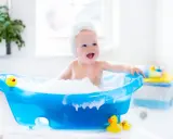 Radosna kąpiel noworodka w pianie, z gumowymi kaczuszkami. Uśmiechnięte dziecko w niebieskiej wanience.