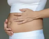 Kobieta dotyka swojego wzdętego brzucha, czując dyskomfort.