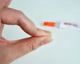 Fingerkuppen kleben zusammen. Ein Röhrchen mit debonder liegt unscharf im Hintergrund.