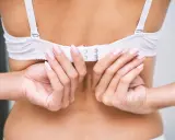 Mani che chiudono un reggiseno bianco, forse un po' troppo grande, mostrando la chiusura posteriore.