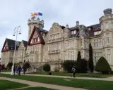 Palacio de la Magdalena en Santander, con banderas ondeando en la torre. Turistas pasean por los jardines de esta joya arquitectónica.