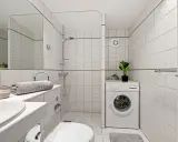 Baño con lavadora, ducha y un extractor de aire en la habitación para mantener la frescura.