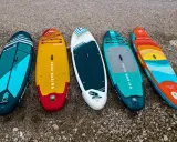 Pięć kolorowych desek z wiosłem leży na plaży. Gotowe na przygodę na wodzie!