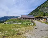 Malga Tuglia, un rifugio alpino con pannelli solari, immerso nel verde con montagne sullo sfondo.
