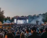 Stor publik vid Rosendal Garden Party. En stor scen med artister och ljus. Rök och träd i bakgrunden.