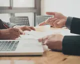 Dwóch mężczyzn w garniturach analizuje dokumenty przy laptopie. Rozpoczynają własną działalność, omawiając strategię.