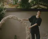 Kajsa Melchior står vid en skulptur i en trädgård.