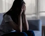 Kobieta siedzi na kanapie, zakrywając twarz dłońmi. Zastanawia się, jakiej śmierci najbardziej się boi, pogrążona w smutku.