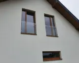 Nowoczesny portfenetr z drewnianymi ramami i szklaną balustradą na białej elewacji.