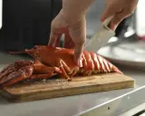 Hand schneidet gekochten Hummer für ein Hummer-Rezept auf einem Holzbrett.