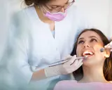 Dentystka w masce i rękawiczkach bada zęby pacjentki za pomocą lusterka i wiertła.