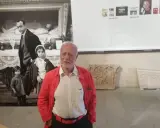 Un uomo anziano con giacca rossa, davanti a una foto di Ferdinando Scianna in Sicilia con bambini.