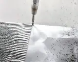 CNC-Fräser bearbeitet eine **Aluminiumstange**, die in Wellen und Rillen geformt wird. Späne bedecken die Oberfläche.
