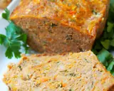 Pyszna pieczeń z mięsa mielonego, pokrojona w plastry, z widocznymi kawałkami marchewki i ziół, udekorowana natką pietruszki.