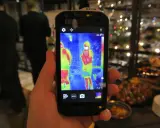 Ręka trzyma smartfon Cat S60 z włączoną termowizją, pokazującą dwie osoby w cieplejszych barwach.