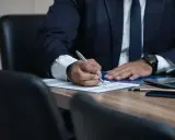 Prawnik w garniturze podpisuje dokumenty przy biurku.
