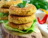 Złociste kotlety z kalafiora na 3 sposoby, podane na liściach sałaty, z parmezanem i natką pietruszki. Obok czerwone i żółte papryczki chili.