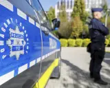 Policjant w mundurze stoi obok radiowozu z widocznym znakiem Policji i numerem 112.