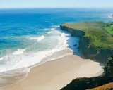 Atemberaubende Küstenlandschaft am Camino del Norte. Grüne Hügel treffen auf das azurblaue Meer mit sanften Wellen, die auf einen einsamen Sandstrand treffen.