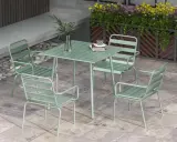 En grön rottingfåtölj utomhus, del av ett cafébord med stolar.