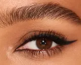 Ojo con pestaña larga y ceja poblada, delineado negro con un sutil eyeliner difuminado en el párpado superior.