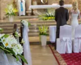 Kwiaty zdobią kościelną nawę. Para młoda stoi przy ołtarzu, przygotowując się do ślubu kościelnego jednostronnego.