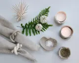 Två ljusstakar av lufttorkande lera med värmeljus, salt- och pepparskålar, servettringar och en dekoration av torkade pumpor på en ormbunksgren.