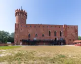 Zamek w Świeciu, ceglana twierdza z wieżą, otoczona zielenią i dziedzińcem.