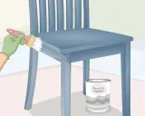 Pintando una silla de madera azul con un pincel. Un bote de sellador acrílico está al lado. Aprende como pintar sillas de madera estilo vintage.