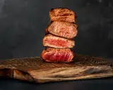 Gestapelte, saftige Steak-Scheiben, perfekt englisch gebraten, auf einem rustikalen Holzbrett.