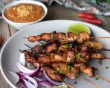 Pyszne satay z kurczaka na patyczkach, podane z sosem orzechowym, limonką i papryczkami chili.