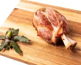 Codillo de cerdo asado, jugoso y dorado, reposa sobre una tabla de madera junto a unas bellotas.