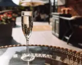 Ein Glas Sekt auf einem Tisch im Freien. Die Bläschen im Glas zeigen, dass der Sekt frisch ist und die Haltbarkeit noch gut ist.