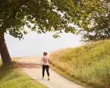 En kvinna går på en grusväg under ett träd. Hur lång tid tar det att gå en mil? Kanske en timme i detta vackra landskap.
