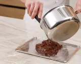 Comment faire fondre du chocolat : une casserole verse du chocolat fondu sur une plaque recouverte de film plastique.