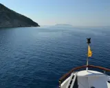 La prua di una barca naviga verso un'isola lontana, un viaggio che evoca la poesia di Itaca.