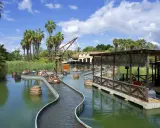 Atracción acuática con barcas y barriles flotantes, ideal para saber donde ir de vacaciones con niños. Palmeras y cielo azul.
