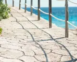 Camino de piedra con barandilla y mar azul. Ideal para aprender como hacer hormigon impreso y crear senderos así.
