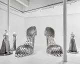 Installazione artistica mostra valentino roma: due enormi scarpe metalliche e abiti da sera su manichini.