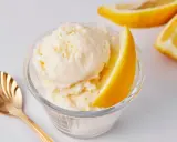 Erfrischendes zitroneneis selber machen: cremiges Eis in einer Glasschale, garniert mit Zitronenspalten und einer goldenen Löffel.