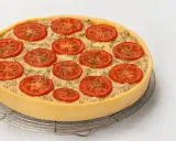 Une délicieuse quiche au thon, garnie de rondelles de tomates fraîches et d'herbes, prête à être dégustée.